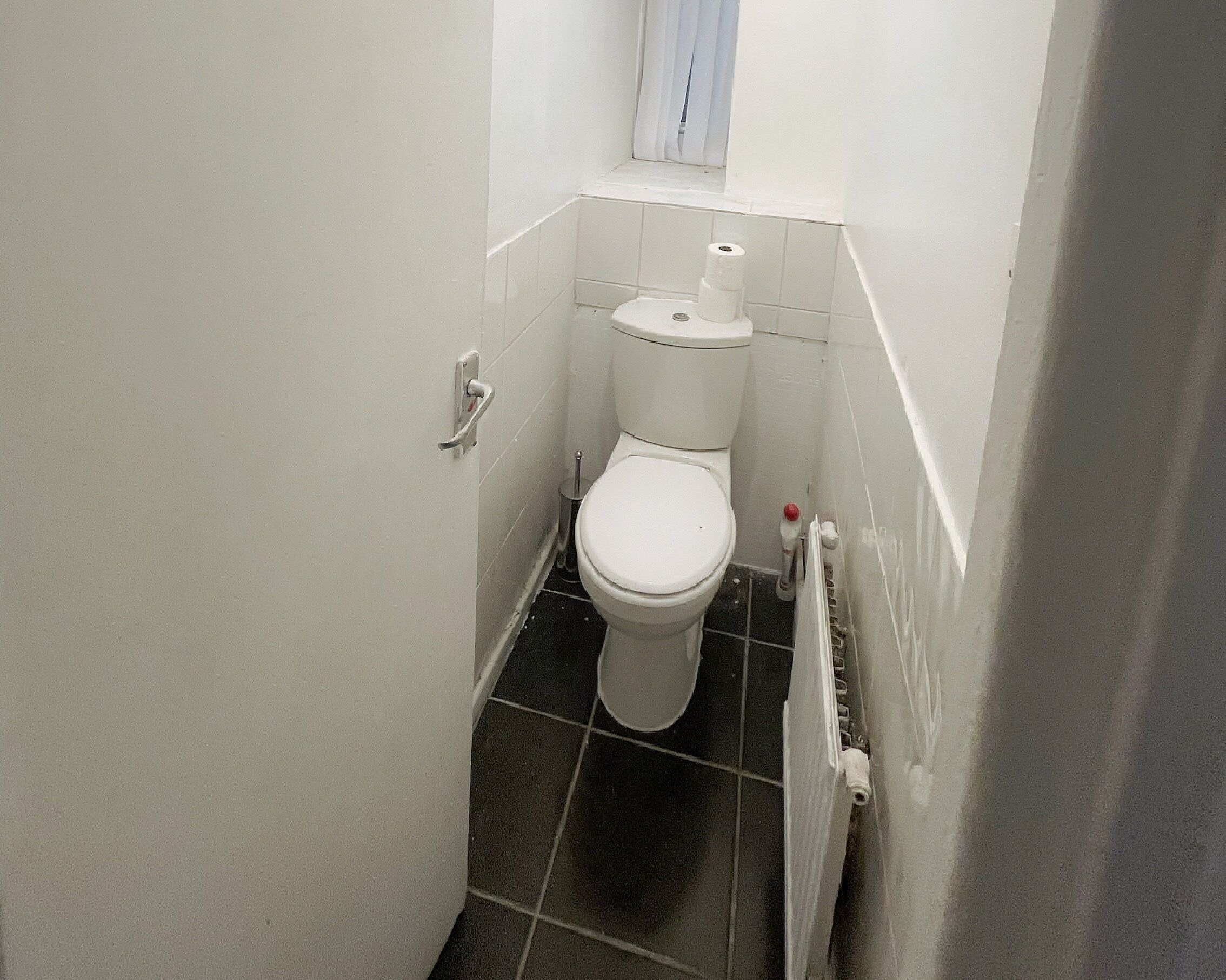 Pieni, käytännöllinen kylpyhuone, jossa on wc, pesuallas ja ikkuna pesualtaan yläpuolella.