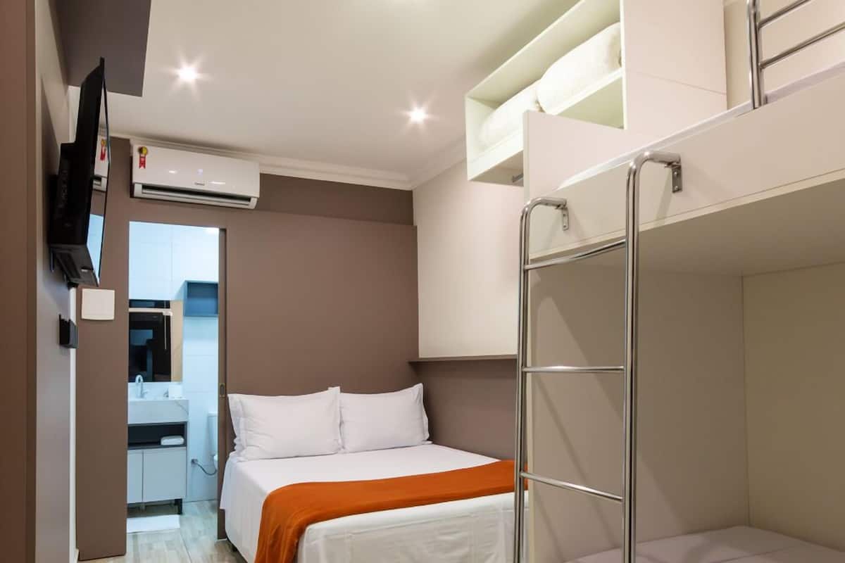 Habitación de hotel compacta con literas, baño pequeño y televisor montado en la pared.