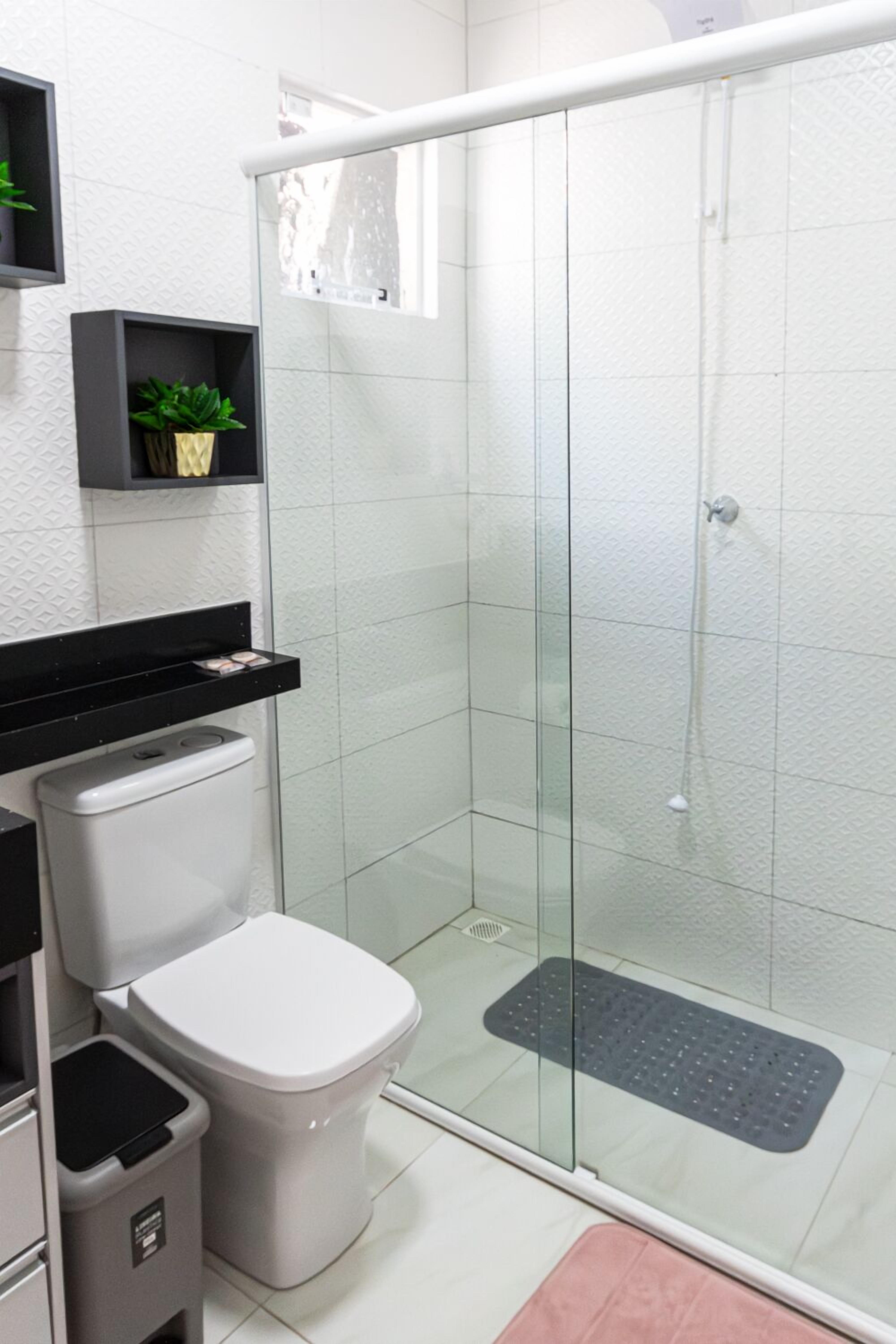 Ein modernes Badezimmer mit einer gläsernen Duschkabine, einer weißen Toilette, einem Mülleimer und einem kleinen Regal mit einer Pflanze.