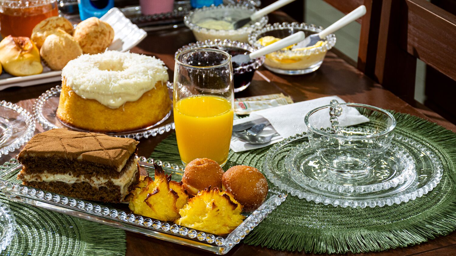 A breakfast table with a variety of pastries, a glass of orange juice, and a decorative glass set.