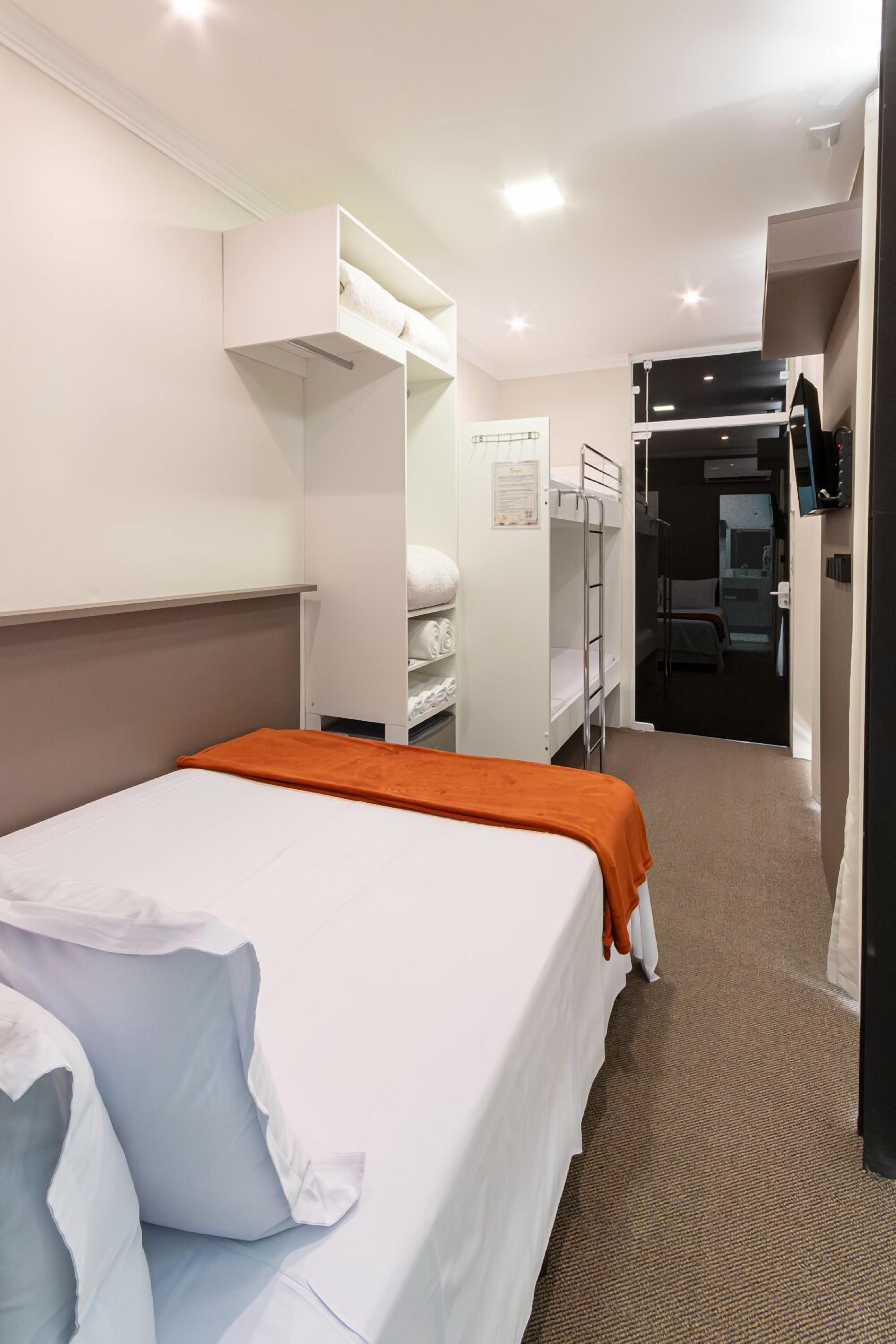 A hotel room with a bed, a wardrobe, a desk, and a bathroom visible through an open door.