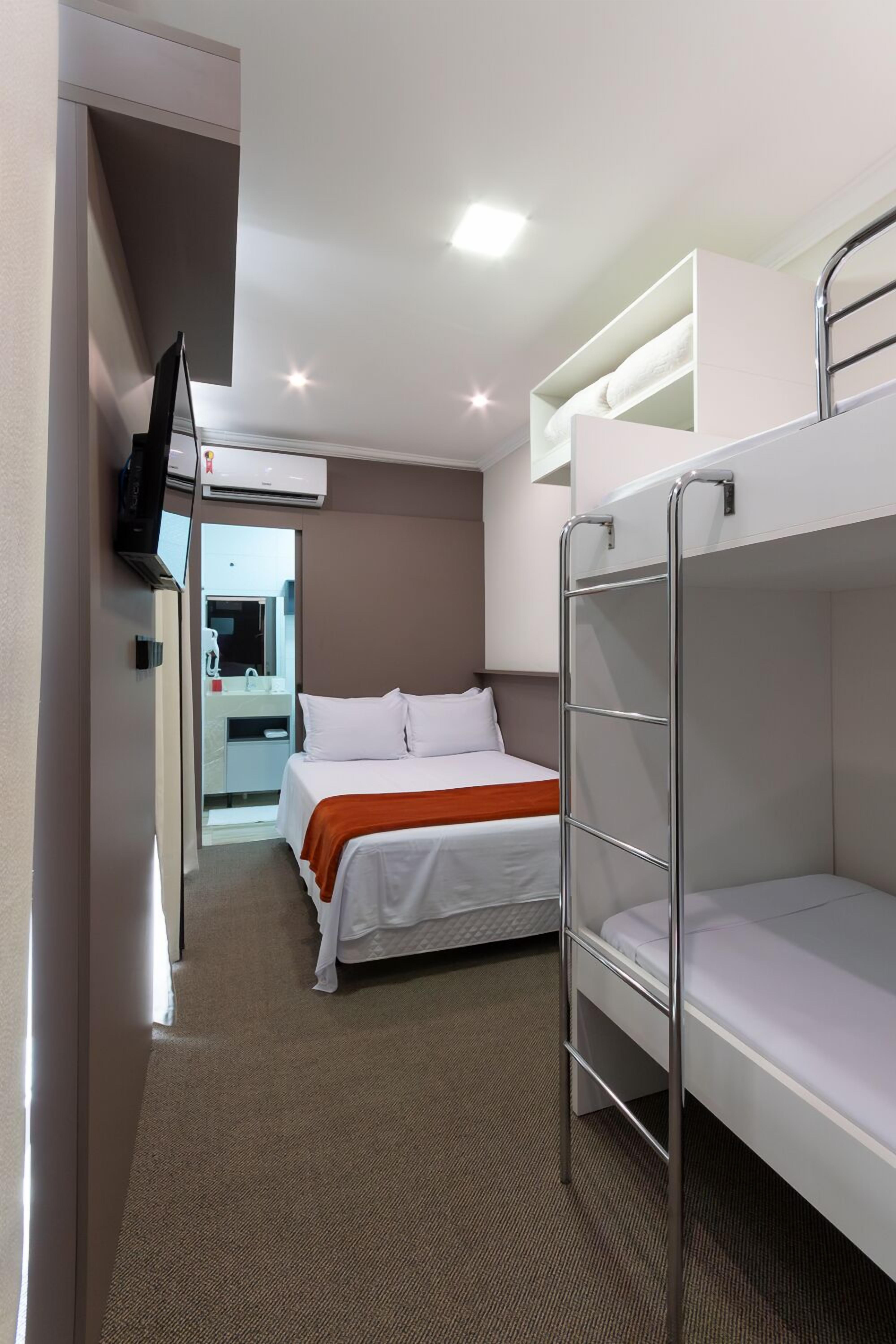 A hotel room with bunk beds, a television, an air conditioning unit, and a bathroom visible through an open door.