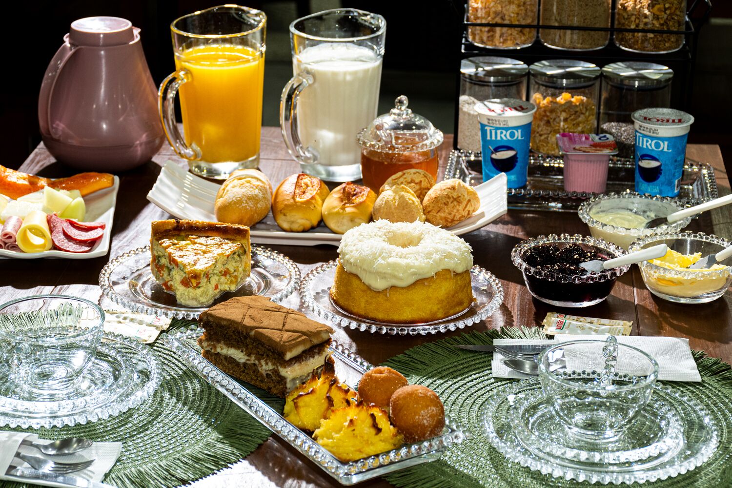 Un bufé de desayuno con diversos pasteles, una jarra de jugo de naranja, una taza de café y recipientes con yogur y cereal.