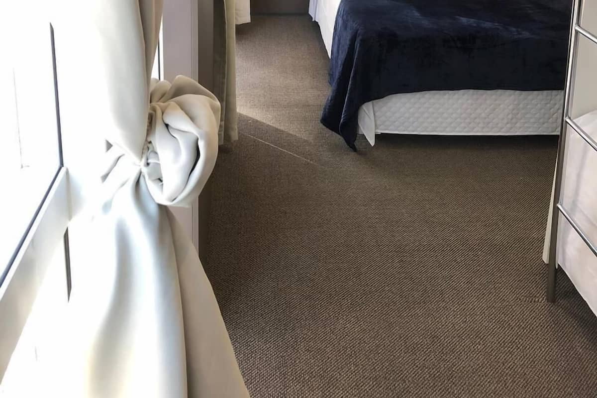 Habitación de hotel con cama, ventana con cortinas, aire acondicionado instalado en la pared y piso alfombrado.