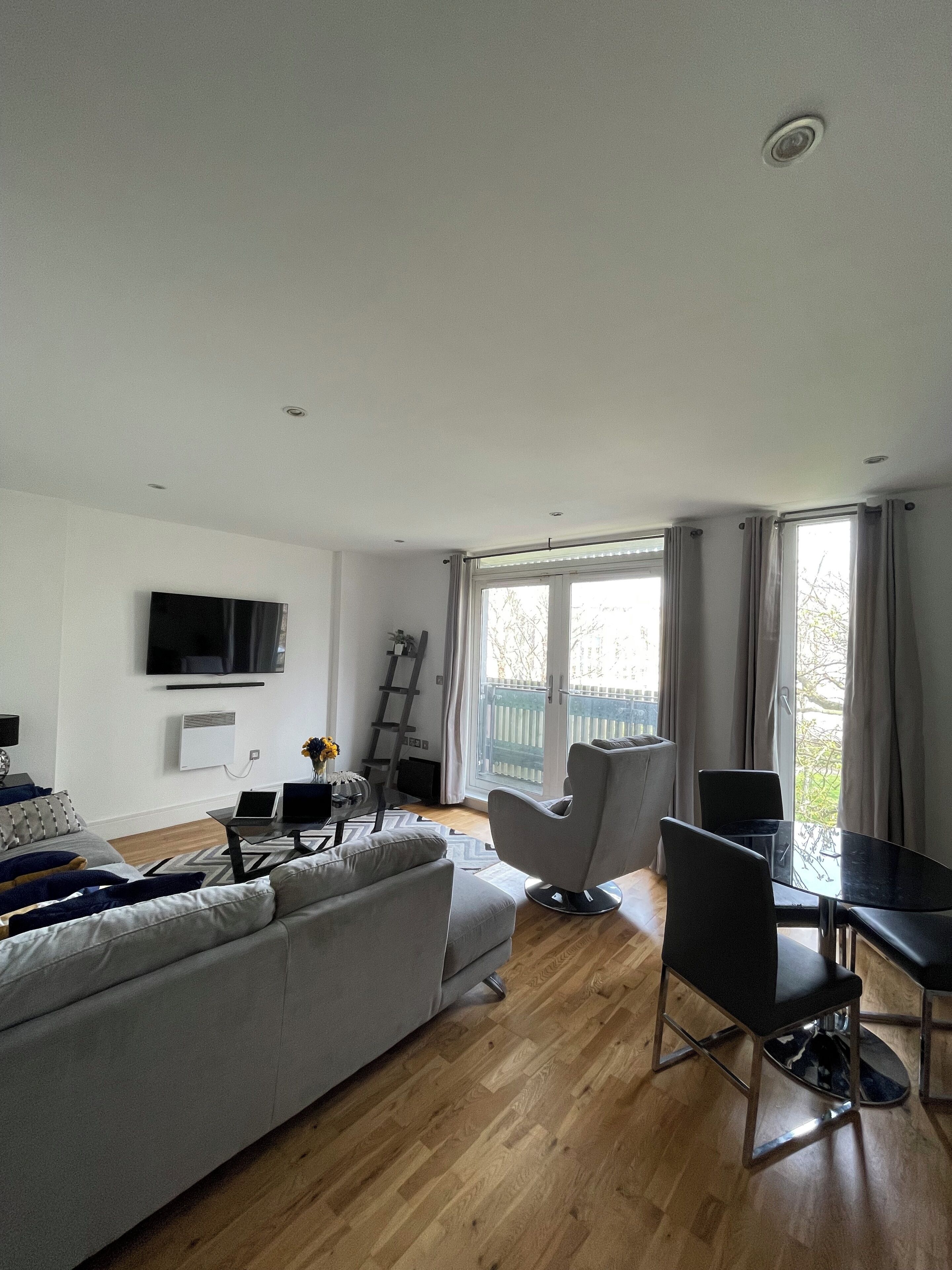 A modern living room with a grey sofa, a glass table, and a TV mounted on the wall.