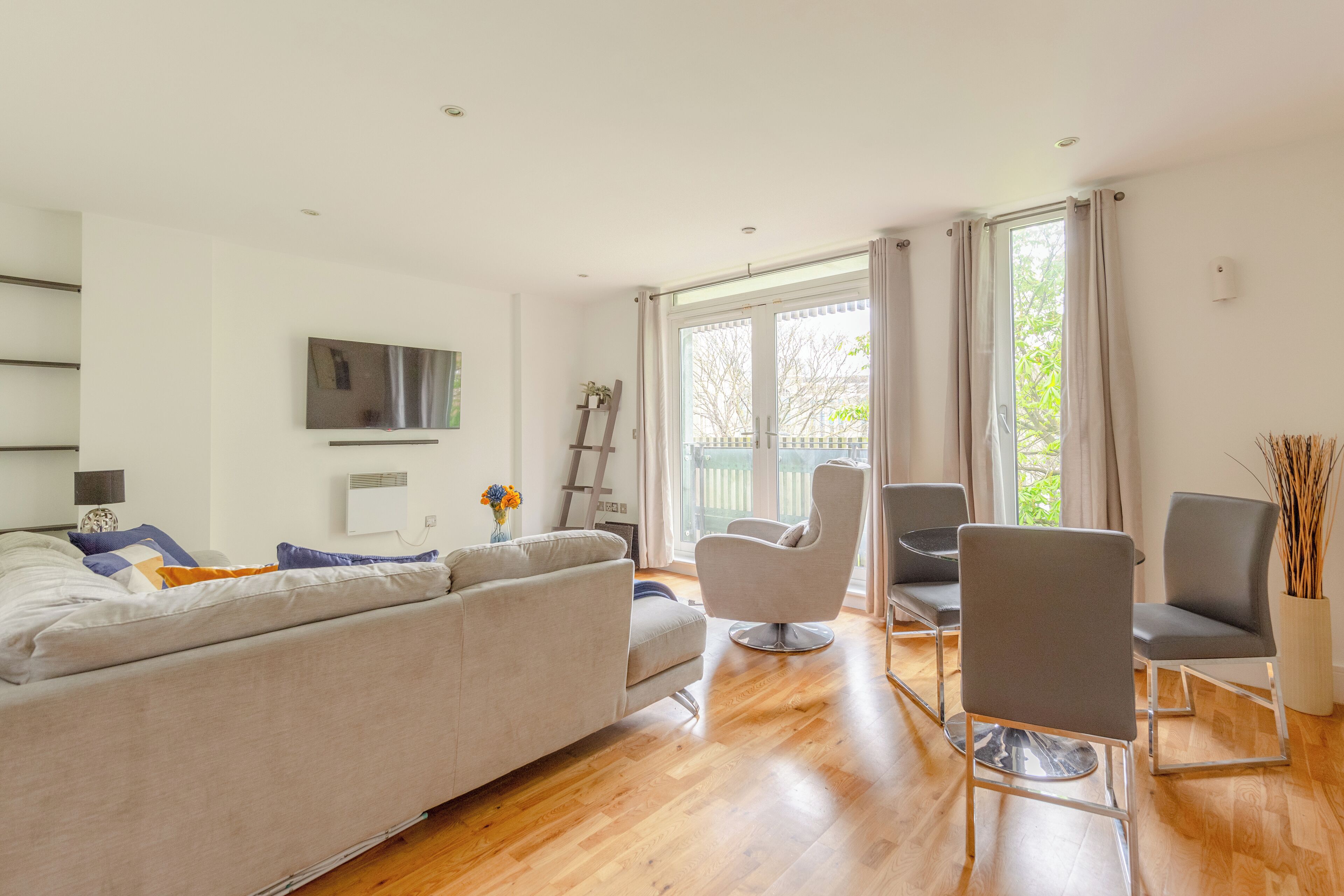 Een moderne woonkamer met een bank, twee fauteuils, een flatscreen televisie en een groot raam met gordijnen.