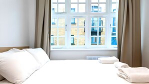 Ein Hotelzimmer mit Bett, Vorhängen, einem Fenster und Blick auf Gebäude.