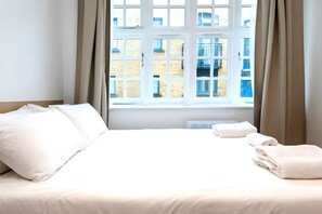 A hotel room with a bed, curtains, a window, and a view of buildings outside. - Newly Renovated 1BD Flat, Heart of Camden (London)