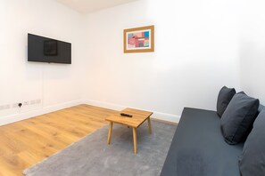 A modern living room with a flat-screen TV mounted on the wall, a small wooden table, a grey sofa, and a grey rug on the floor. - Newly Renovated 1BD Flat, Heart of Camden (London)