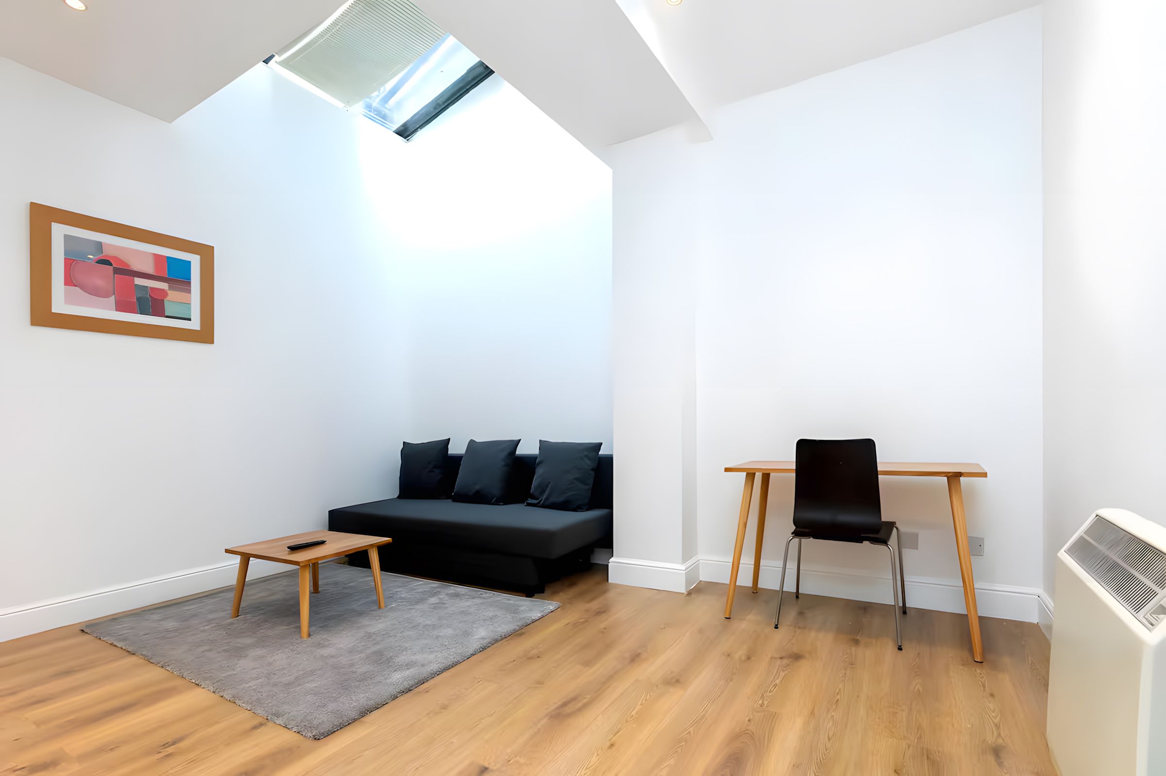 Ein modernes Wohnzimmer mit einer schwarzen Couch, einem kleinen Holztisch, einem schwarzen Sessel und einem grauen Teppich.