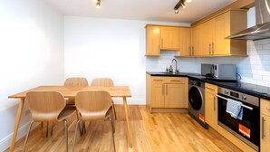 Eine moderne Küche mit Holzausstattung, einem Esstisch mit Stühlen, einer Waschmaschine und einer Mikrowelle.