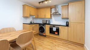 Eine moderne Küche mit Holzausstattung, einer Waschmaschine, einem Backofen und einem Essbereich mit Tisch und Stühlen.
