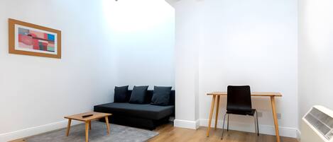 Una sala de estar moderna con un sofá negro, una pequeña mesa de madera, una silla negra y una alfombra gris.