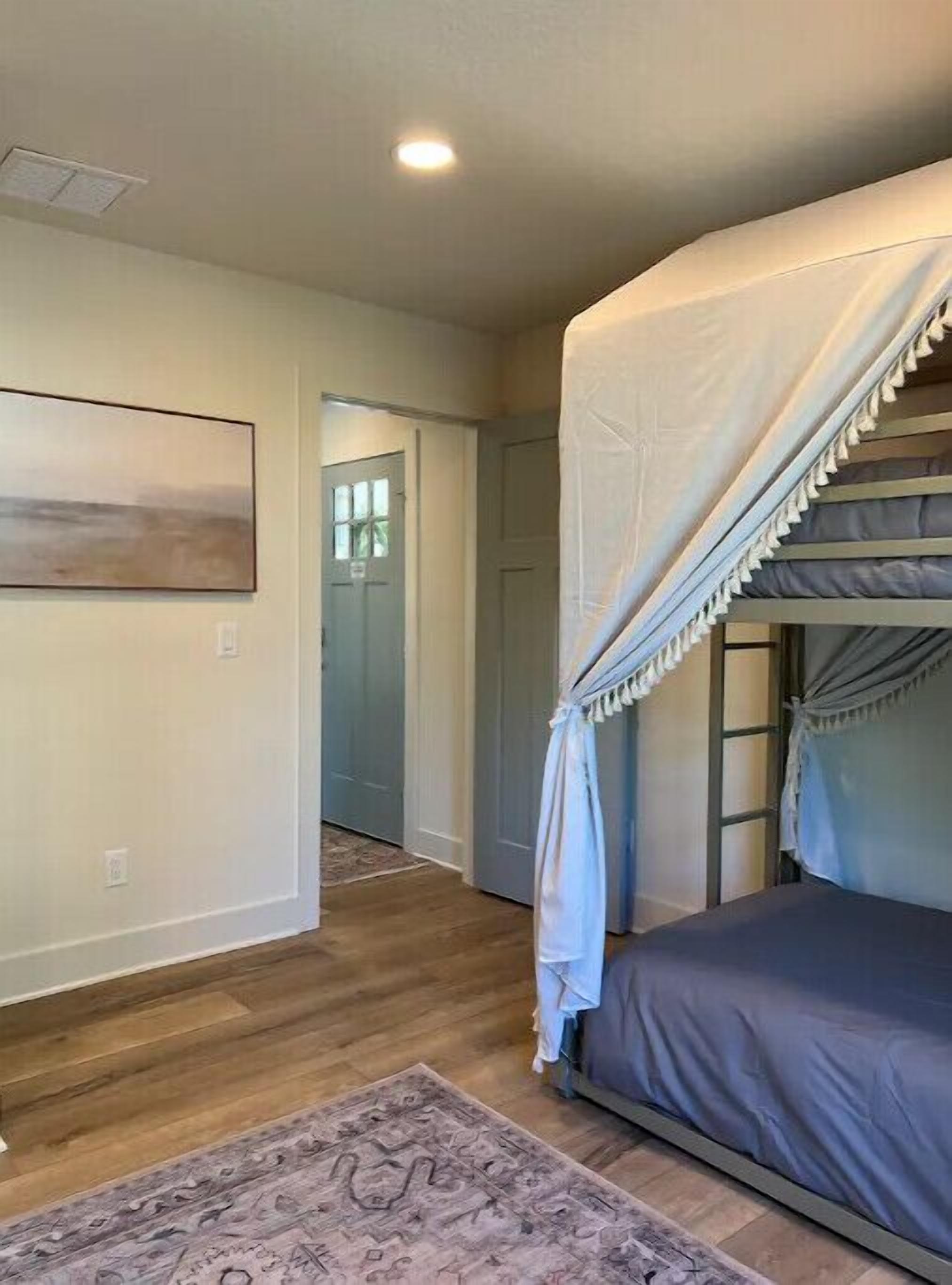 A bedroom with a bunk bed, a ceiling fan, a rug, and a door leading to another room.