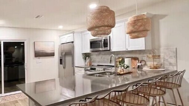A modern kitchen with a central island, bar stools, and hanging light fixtures.