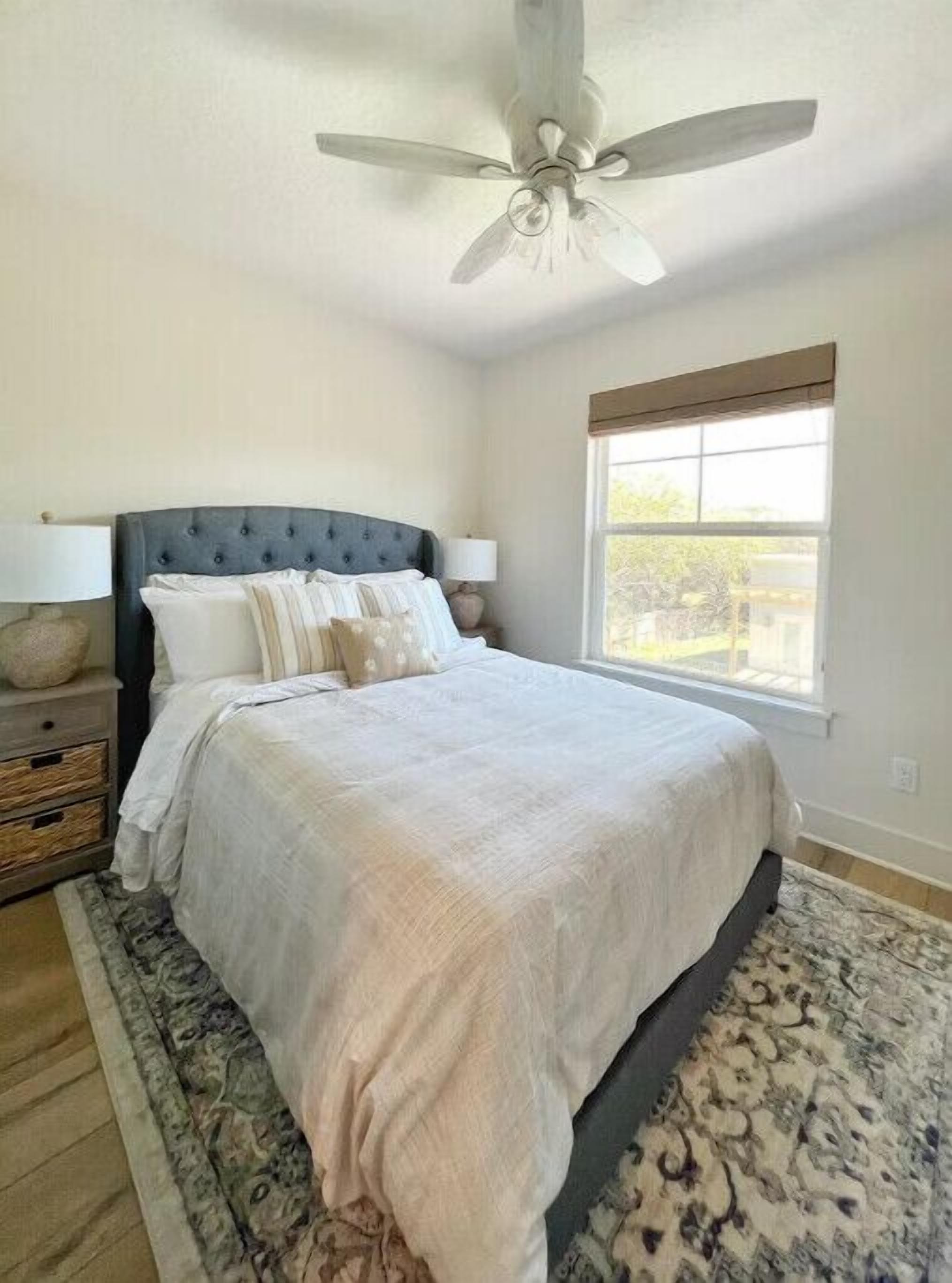 Une chambre avec un grand lit, un ventilateur de plafond, une fenêtre donnant sur un beau paysage et une table de chevet avec une lampe.