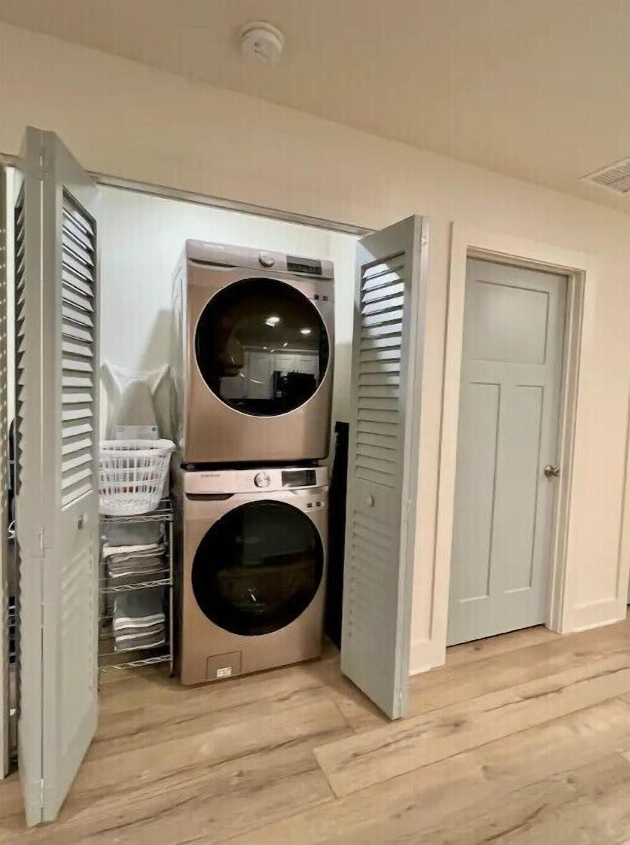 A laundry room with two stacked washers and dryers, a white basket, and a door to another room.