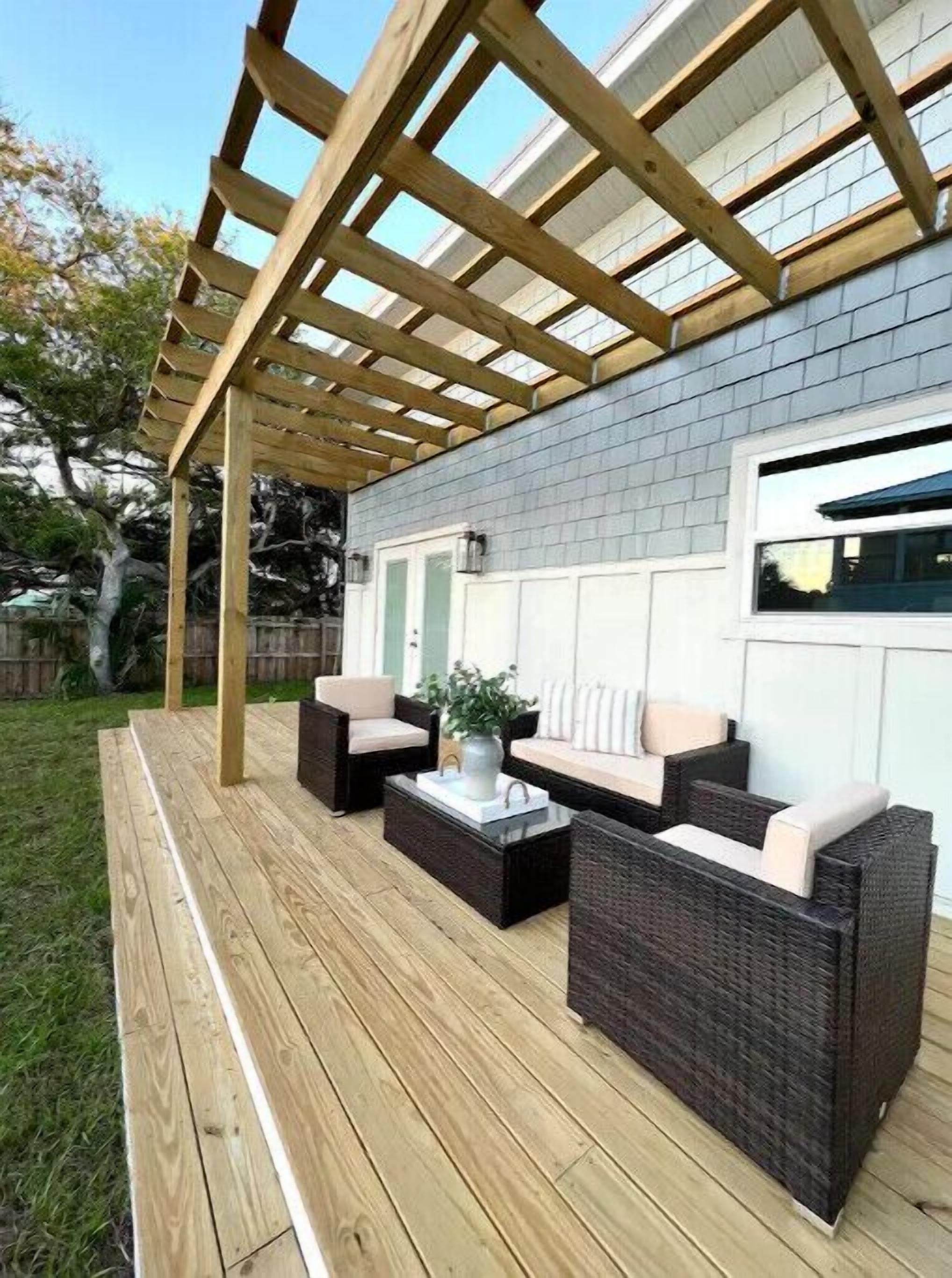 A covered patio with outdoor furniture, a wooden deck, and a grey brick wall.