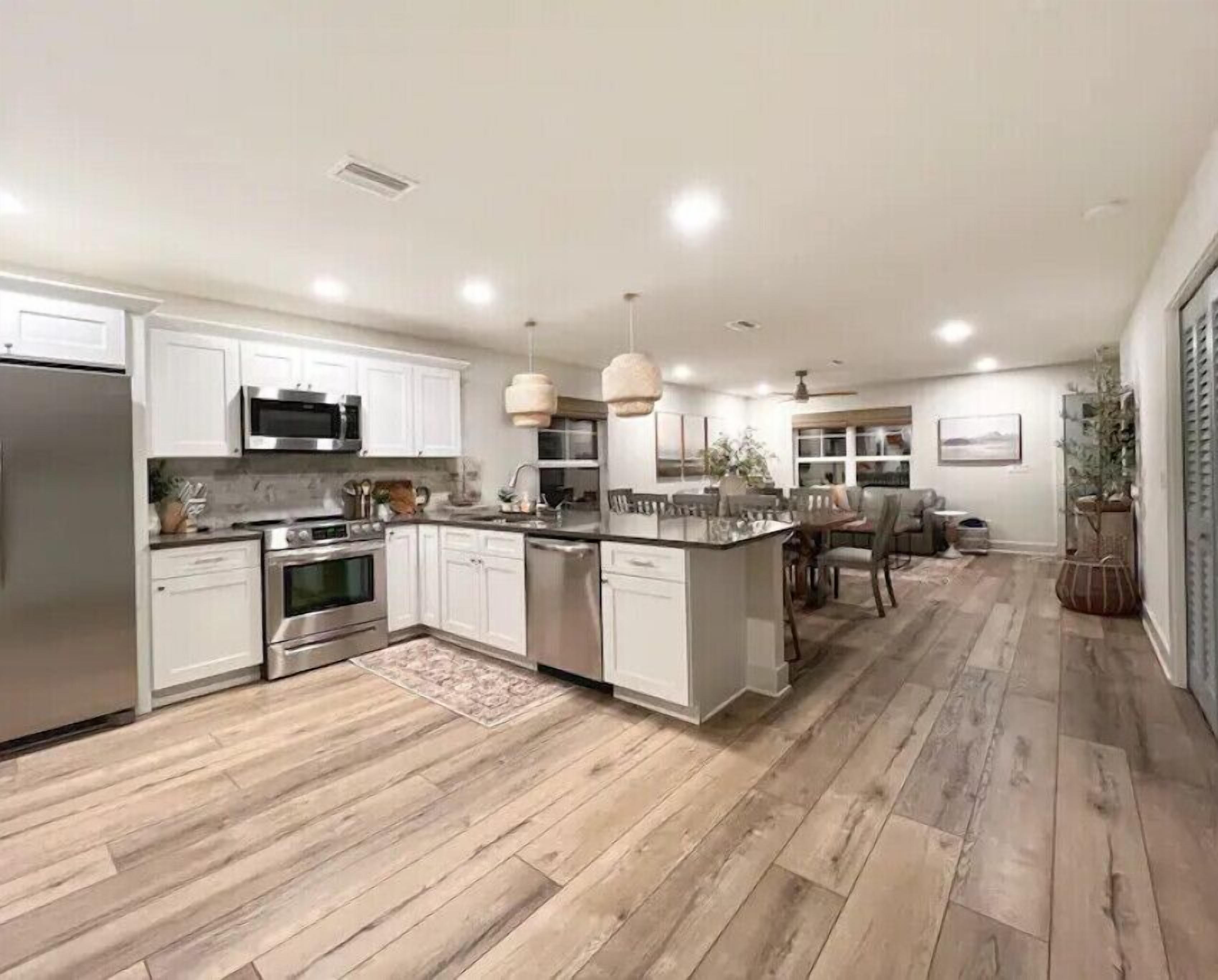 Una cocina moderna con armarios blancos, electrodomésticos de acero inoxidable y piso de madera.