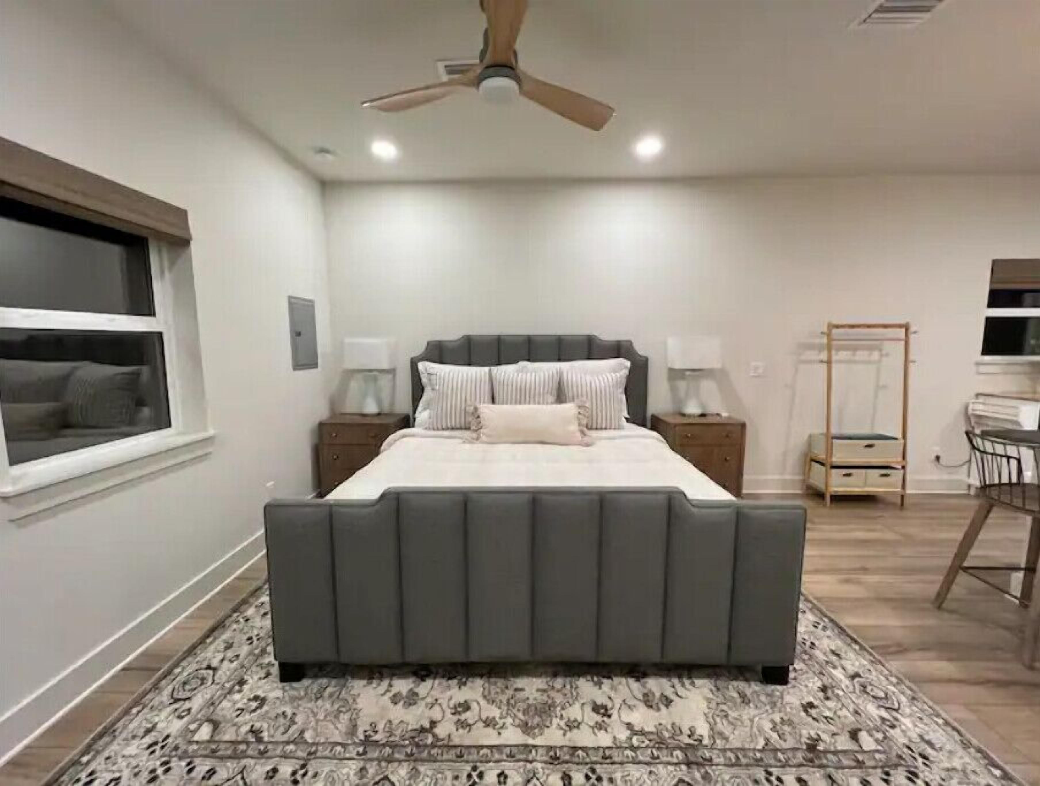Une chambre à coucher avec un grand lit, un ventilateur de plafond, des lampes de chevet, une table de chevet, une armoire et une fenêtre.