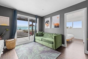 Una habitación moderna con un sofá verde, una cama, un ventanal grande y obras de arte en las paredes.