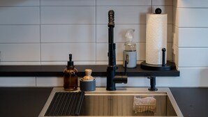 A kitchen with a wooden countertop, a sink, a potted plant, a bottle, a soap dispenser, and a roll of paper towels.