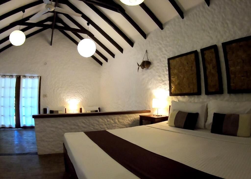 Une chambre avec un grand lit, un ventilateur de plafond et une fenêtre avec des rideaux.
