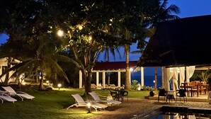 A poolside area with lounge chairs, a pool, and a building with a red roof. - Casa Amihan (Anda)