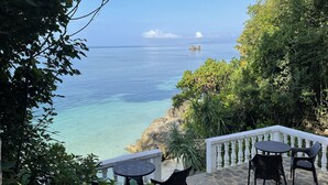 A patio with stone flooring and black wicker furniture, overlooking a clear blue sea and rocky coastline. - Casa Amihan (Anda)