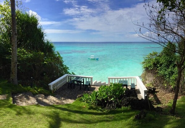 A view of a beach with a boat in the water, a white fence, and a grassy area leading to the water. - Casa Amihan (Anda)