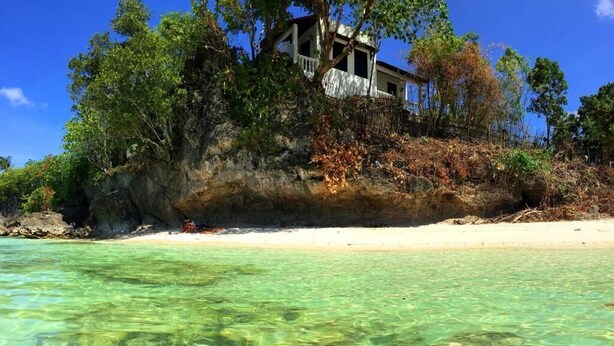 A beachfront property with clear water, a sandy beach, and a building surrounded by trees. - Casa Amihan (Anda)