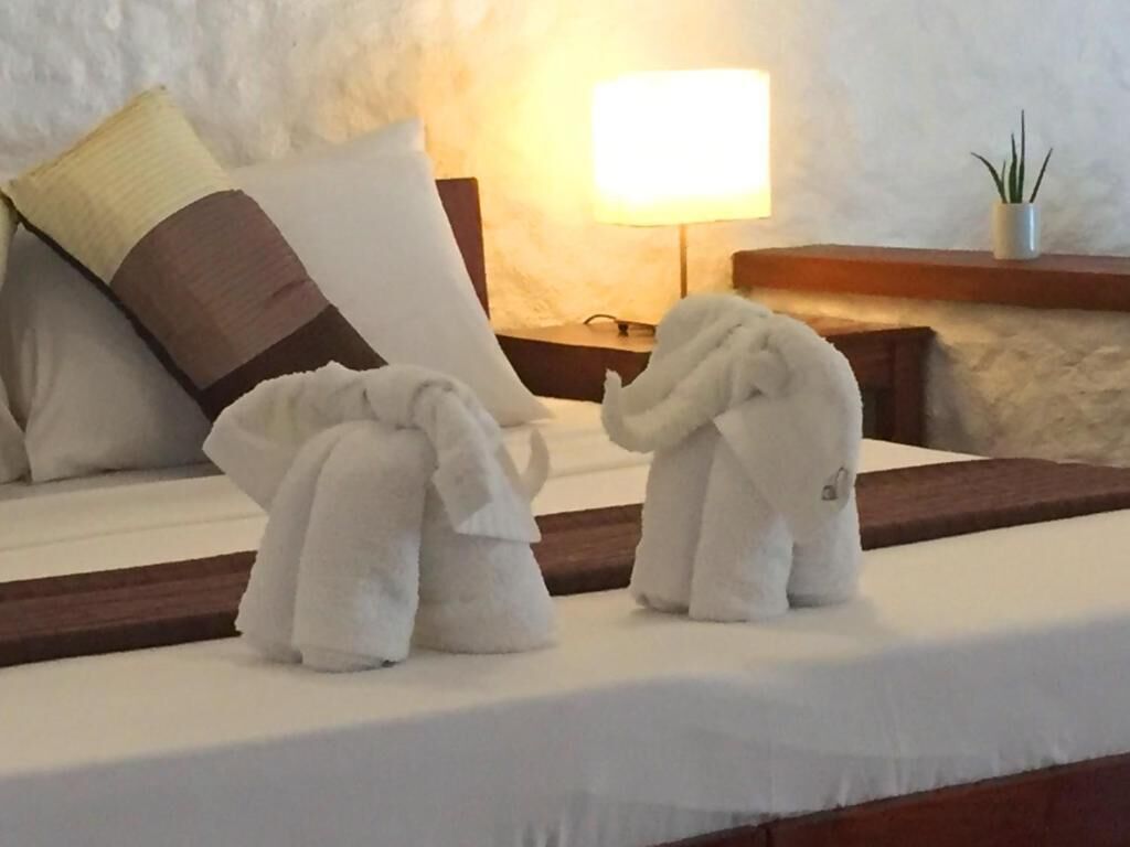 A hotel room with a bed, pillows, a nightstand, a lamp, and a potted plant.