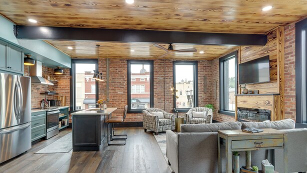 Una cocina moderna con techo de madera, ventanas amplias y una zona de estar con sofá y sillones.