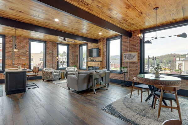 A spacious living area with a large window, a fireplace, a dining table, and a kitchen area with a bar.