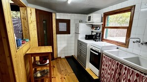 Une cuisine compacte avec un plancher en bois, des murs recouverts de carreaux blancs, un four encastré, un four à micro-ondes et un évier.