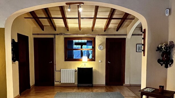 Un couloir voûté avec des poutres en bois, un radiateur, une horloge et une petite table sur laquelle se trouve un vase.