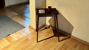 Une pièce avec un plancher en bois, une petite table sur laquelle est posé un vase de fleurs, un miroir et une enseigne en bois accrochée au mur.