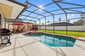 Une piscine extérieure couverte avec un espace patio comprenant un barbecue et des sièges.