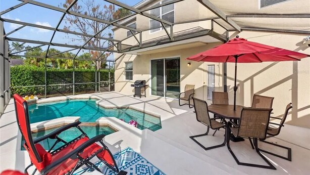 Un espace piscine protégé par une paroi en verre, une table à manger avec des chaises et un parasol rouge.