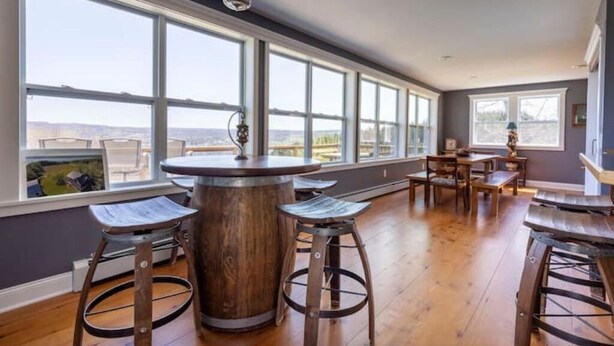 Een ruime kamer met grote ramen, een ronde houten tafel en barkrukken.
