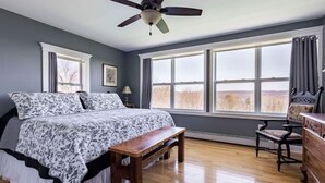 Een slaapkamer met een bed, een houten bankje, een stoel, een dressoir en een plafondventilator.