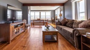 Een ruime woonkamer met een houten vloer, een bank, een salontafel en een televisie.
