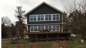 Een tweelaags huis met een terras, omringd door een vuurkorf en houten stoelen.