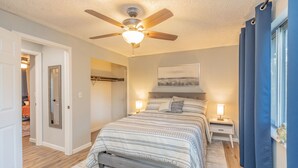 Une chambre à coucher avec un lit, des lampes de chevet, un ventilateur de plafond, une porte et une fenêtre avec des rideaux.