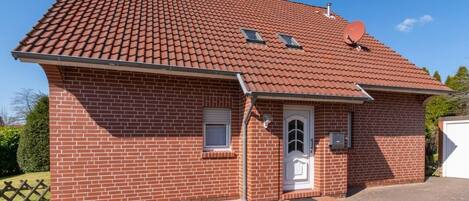 Una casa de maó de dos pisos amb teulada vermella, antena parabòlica i una finestra petita.