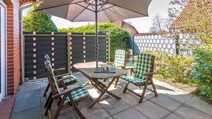 Een buitenterras met een tafel, vier stoelen, een parasol en een bakstenen muur.