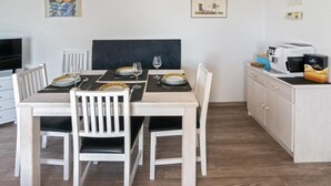 Een eethoek met een tafel voor vier personen, witte stoelen, een zwarte met kussens uitgevoerde bank en een magnetron op het aanrecht.