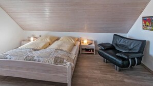 Een slaapkamer met een houten bed, nachtkastjes, een zwarte leren fauteuil en een kleurrijk kunstwerk aan de muur.