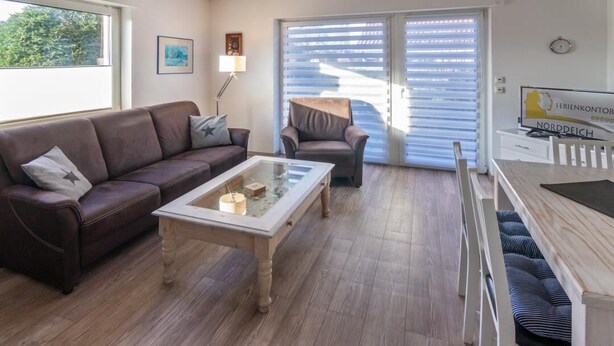 Een woonkamer met een bruine leren bank, een glazen salontafel en een houten eettafel met banken.