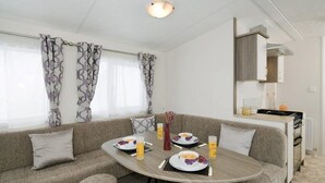 Een moderne, goed verlichte kamer met een bank, eettafel en kitchenette.